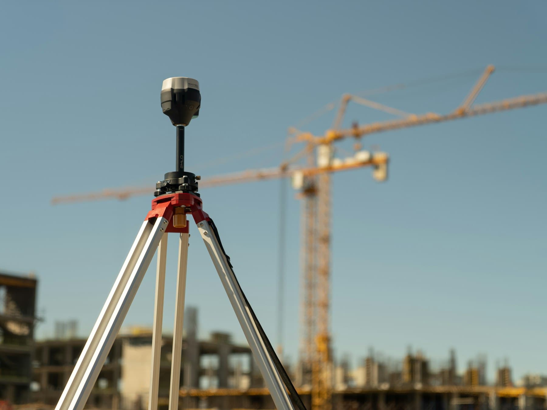Şantiyede tripod üzerinde ölçüm cihazı ve arkada kule vinç
